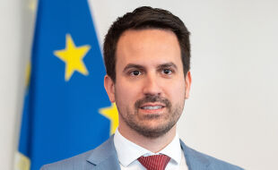 Christoph Wiederkehr, Bildungsminister (NEOS) - Zu sehen ist Christoph Wiederkehr (Bildungsminister) von vorne, hinter ihm eine blau-gelbe EU-Flagge