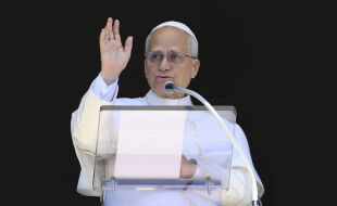Papst Leo XIV. - Der Papst in typischer weißer Kleidung und Pileolus hebt bei einer Ansprache grüßend die rechte Hand - © APA / AFP / Vatican Media / Handout