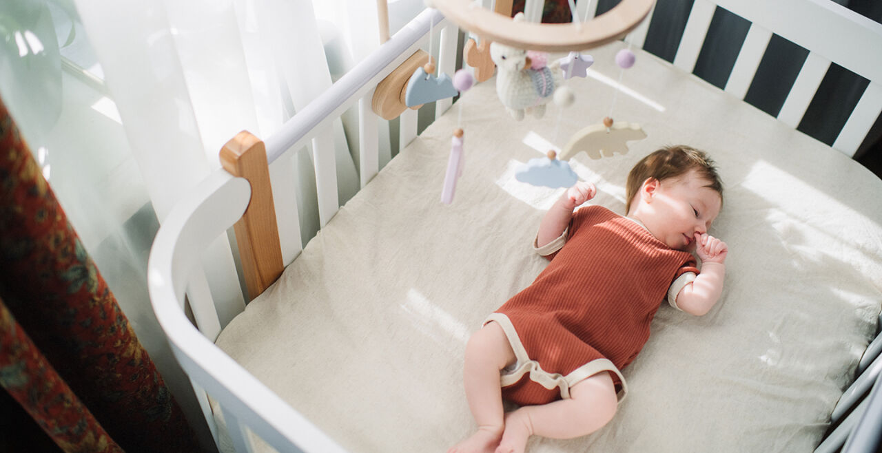 Ein Baby in einem Gitterbett - Das Foto zeigt ein Baby einem roten Strampler, das in einem Gitterbett schläft. - © iSock/ArtMarie