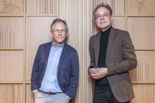 Doron Rabinovici und Jan-Heiner Tück - Zwei Männer stehen vor einem hölzernen Bücherregal mit mehreren Fächern, beide tragen Sakko und Hemd, einer in Blau, der andere in Braun. - © Foto: Carola Frank