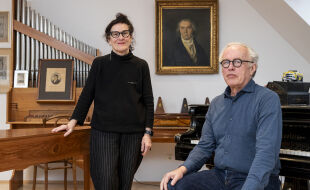 Elisabeth Schweeger Martin Haselböck - Elisabeth Schweeger und Martin Haselböck in einem Raum mit Klavier und historischen Porträts an der Wand, eine Person steht, die andere sitzt. - © Foto: Carolina Frank