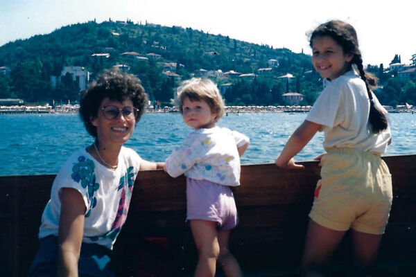 Familie Renner - Eine Mutter und zwei Kindern stehen an einem hölzernen Geländer mit Blick auf das Meer und einen bewaldeten Hügel im Hintergrund. - © Foto: PrivatDrei Kinder stehen an einem hölzernen Geländer mit Blick auf einen See und bewaldeten Hügel im Hintergrund