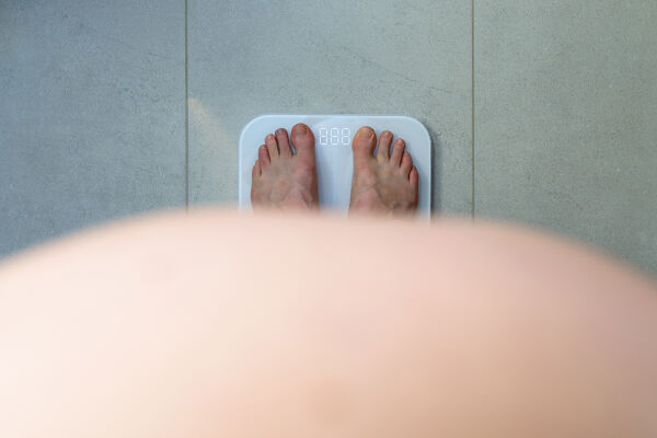 Adipositas Übergewickt dick Bauch - Blick von oben auf nackte Füße auf einer digitalen Waage vor einem runden Bauch - © Foto: Adobe Stock / bubutu
