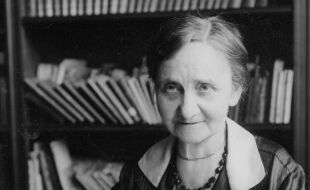 Gabriele Possanner - Schwarz-Weiß Foto von Gabriele Possanner. Sie trägt eine dunkle Bluse mit weißem Kragen und zwei Ketten. Ihre Haare sind am Hinterkopf zusammengebunden. Im HIntergrund ist ein großes Bücherregal zu sehen.  - © Foto: APA-Images / ÖNB-Bildarchiv / ONB Bildarchiv Austria 