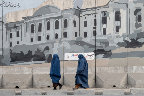 Frauen in Afghanistan - Zwei Frauen in blauen Burkas gehen in Afghanistan an einer Wand mit einem großflächigen Graffiti eines Gebäudes vorbei. - © Foto: APA / AFP / Wakil Kohsar