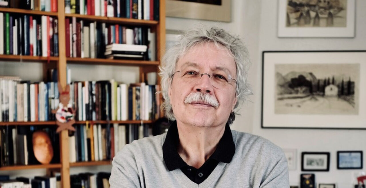 Gauß - Älterer Mann mit Schnauzbart, Brille und dichtem, grauem Haar, blickt leicht lächelnd und mit verschränkten Armen in die Kamera. Hinter ihm hängen mehrere Bilder, vermutlich Bleistiftzeichnungen, außerdem ist ein Bücherregal zu sehen. - © Foto: Stefan Winkler