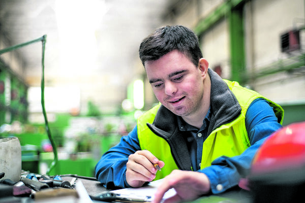 Ein Mensch mit Behinderung bei der Arbeit - Das Foto zeigt einen jungen Mann mit Behinderung in Blaumann und Sicherheitsweste bei der Arbeit.  - © Adobe Stock / Halfpoint