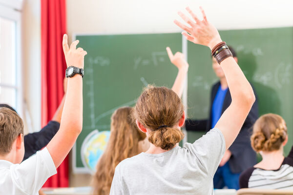 Schulklasse, Unterricht - Das Foto zeigt Schülerinnen und Schüler in einem Klassenzimmer von hinten, während sie aufzeigen.  - © Adobe Stock / Kzenon