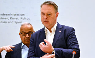 Andreas Babler und Andy Kaltenbrunner Medienförderung Neu - Medienminister und Vizekanzler Andreas Babler (SPÖ) bei der Präsentation der Studie des Medienhauses Wien für eine neue Medienförderung. Babler trägt ein dunkelblaues Jackett und ein weißes Hemd. Mit seiner rechten Hand richtet er seinen linken Ärmel. Im Hintergrund ist Andy Kaltenbrunner, der Chef des Medienhauses Wien, zu sehen. Er trägt eine schwarze Brille, ein dunkelblaues Jackett und ein hellblaues Hemd. Neben ihm ist die Hand einer Frau zu sehen, die mit dem Zeigefinger nach links zeigt. - © Foto: APA / Hans Klaus Techt