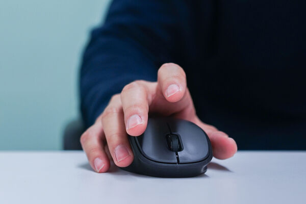 Computermaus Technik  - Hand, die eine schwarze Computermaus auf einem weißen Tisch hält - © Foto: Adobe Stock / chinnarach