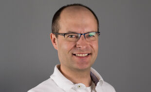 Gerold Muhri, Palliativmediziner, Elisabethinen - Das Porträtfoto zeigt Gerold Muhri mit Brille und in weißem Hemd vor braun-grauem Hintergrund. - © KHE Graz