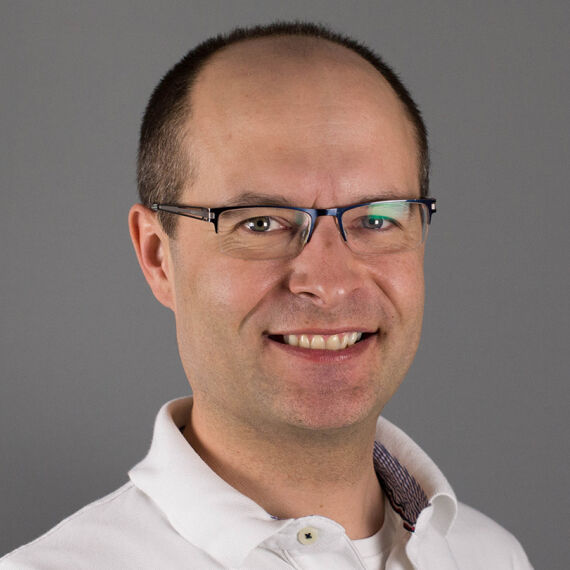 Gerold Muhri, Palliativmediziner, Elisabethinen - Das Porträtfoto zeigt Gerold Muhri mit Brille und in weißem Hemd vor braun-grauem Hintergrund. - © KHE Graz